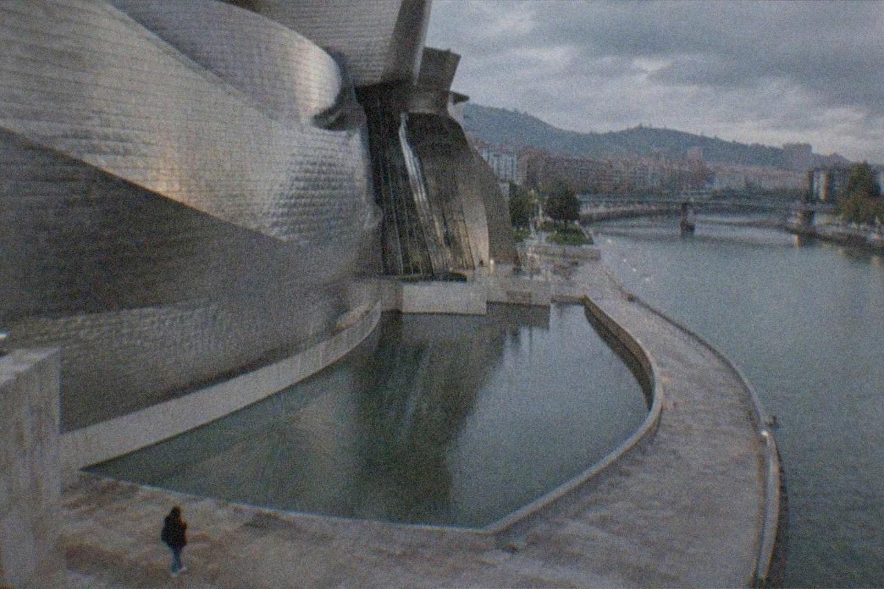 A visitor checking a phone beside the Guggenheim Museum Bilbao on a bright morning