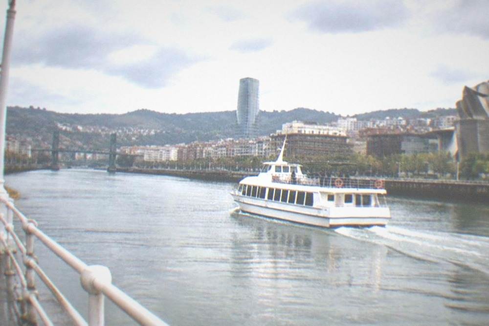 A ferry boat crossing the Nervion estuary with the city skyline behind it