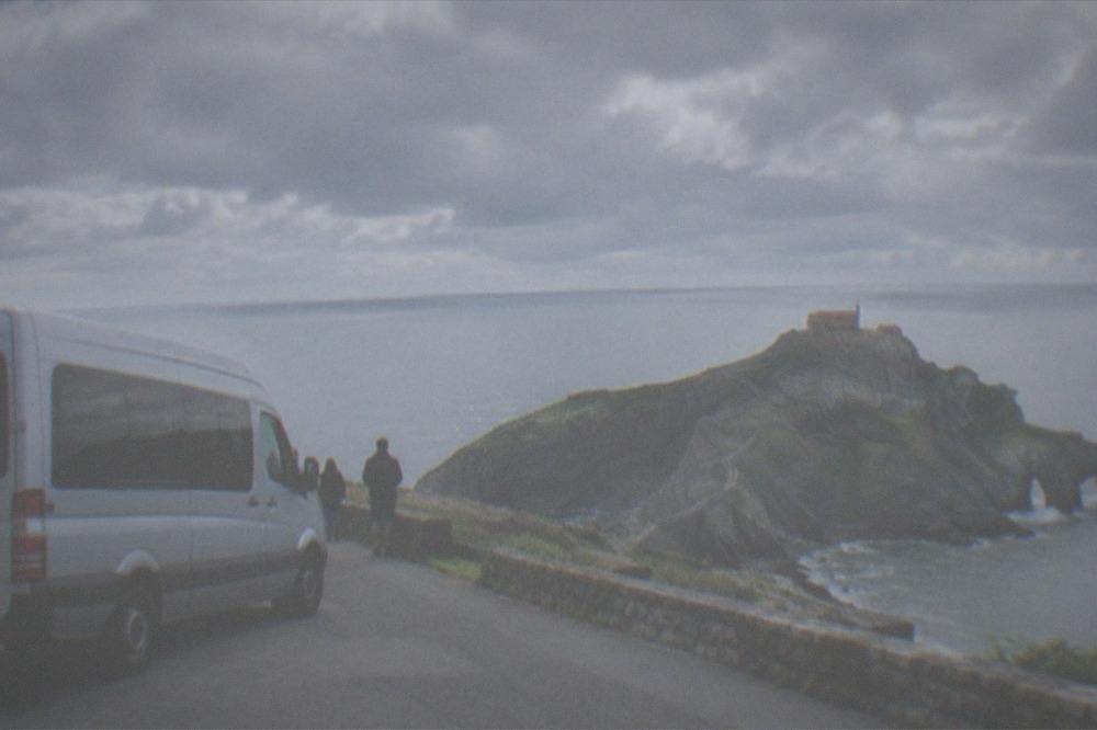 A tour van parked on a coastal road above the Gaztelugatxe islet in Bizkaia