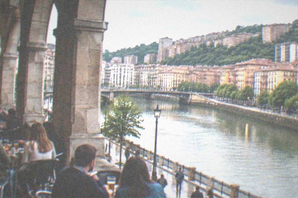 People drinking at outdoor tables under the arcades of a Bilbao square on a warm evening