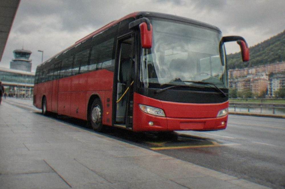 A red Bizkaibus airport bus parked at a stop outside Bilbao Airport terminal