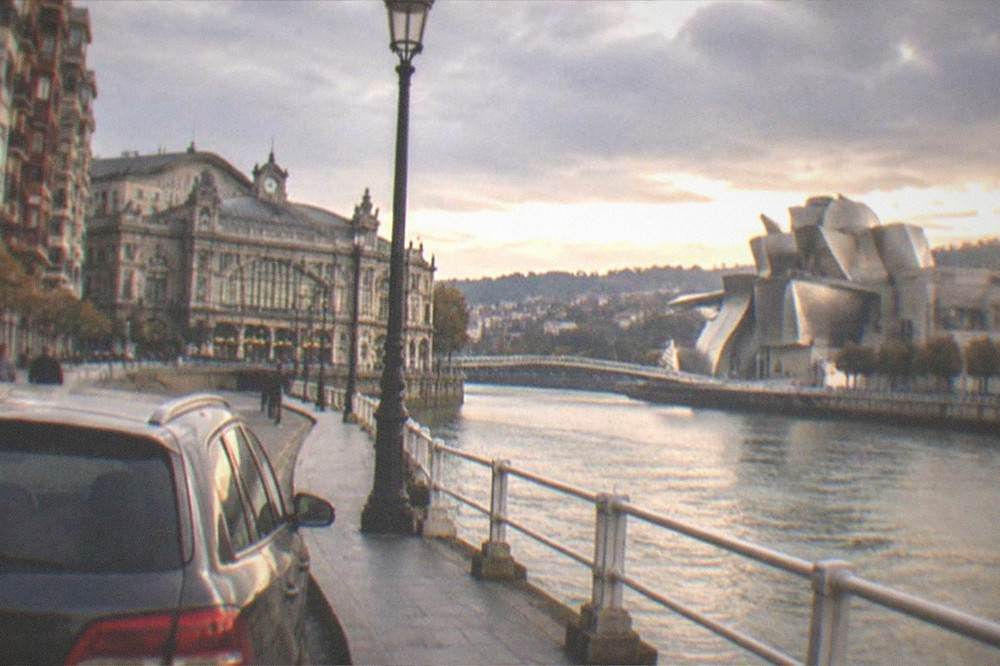 A parked car beside the estuary promenade with the Guggenheim Museum's titanium curves behind