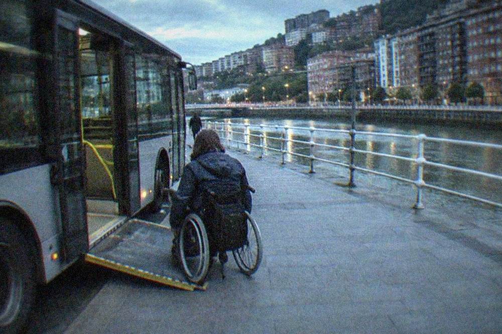 A low-floor Bilbao city bus kneeling at a curb with its ramp extended toward a passenger