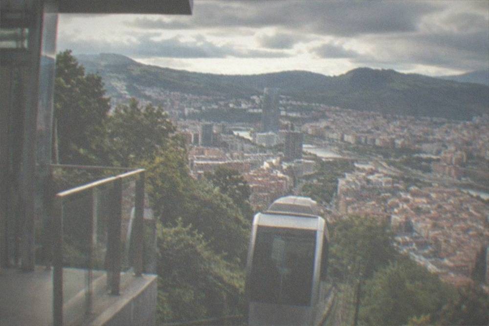The upper platform of the Artxanda funicular station with a lift door and a panoramic view over Bilbao's rooftops