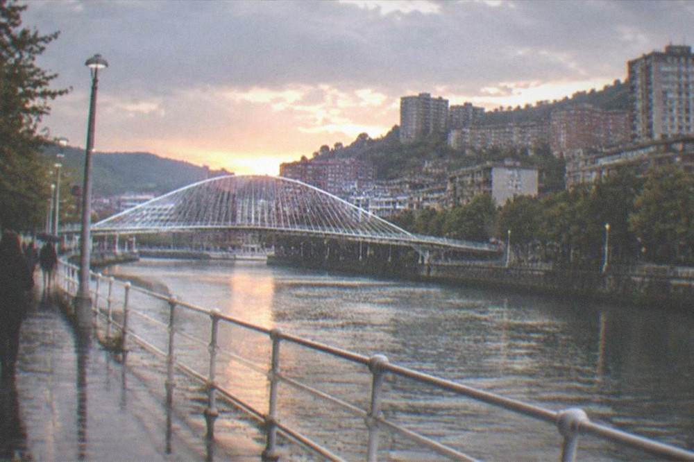 The level stone promenade along the Bilbao estuary at sunset with the Zubizuri footbridge in the distance