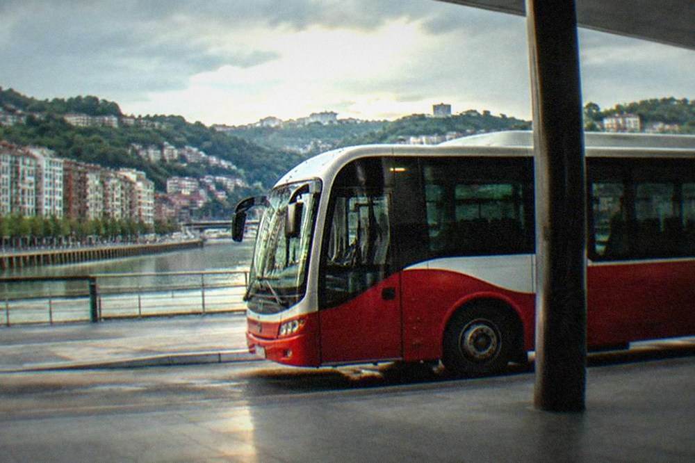 A red and white airport shuttle bus parked at a curb outside a terminal building