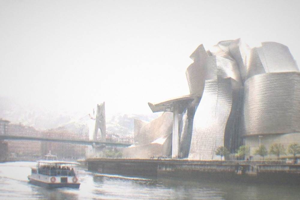 The Guggenheim Museum's titanium curves beside the Nervion river under a partly cloudy sky