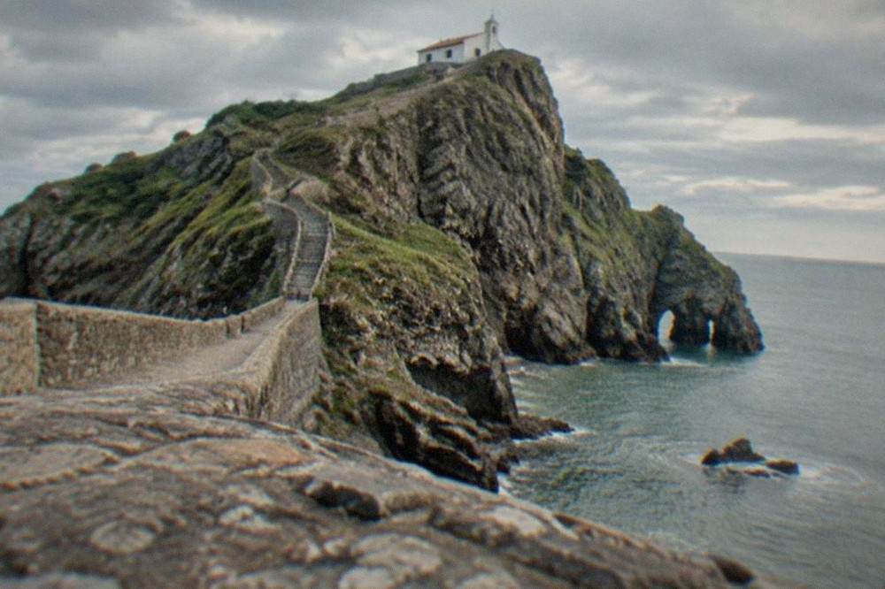 A long narrow stone stairway climbing the side of a rocky island toward a small whitewashed chapel