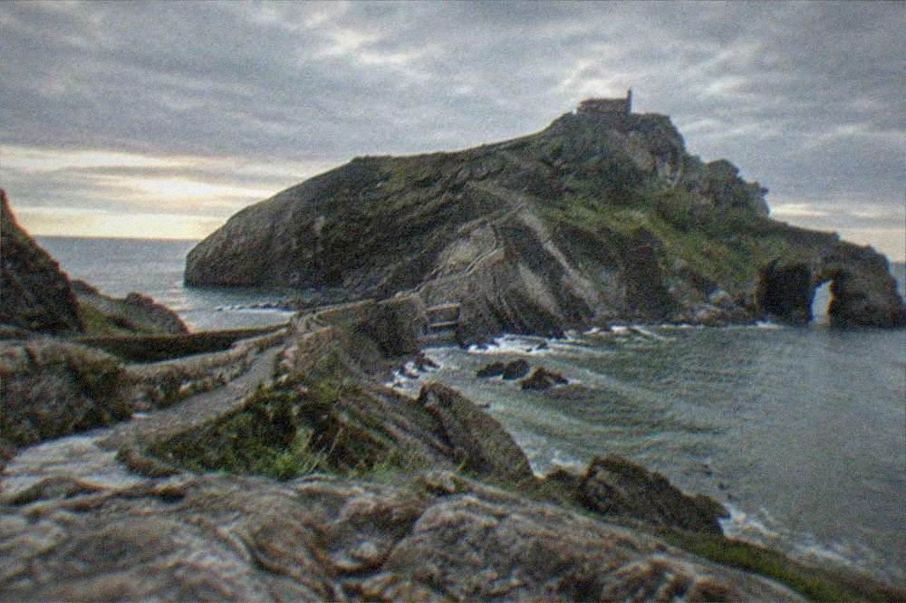 A panoramic view of a rocky coastal islet with a causeway under an Atlantic sky at dusk