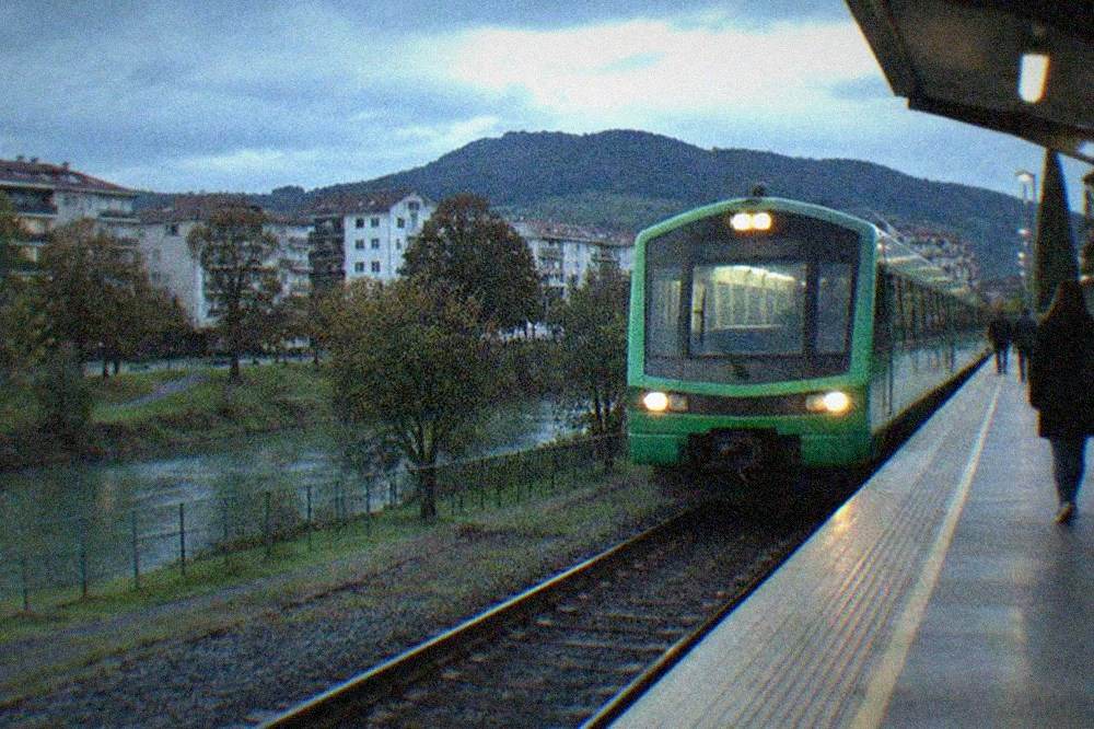 A green regional train arriving at a small station platform in the Basque Country