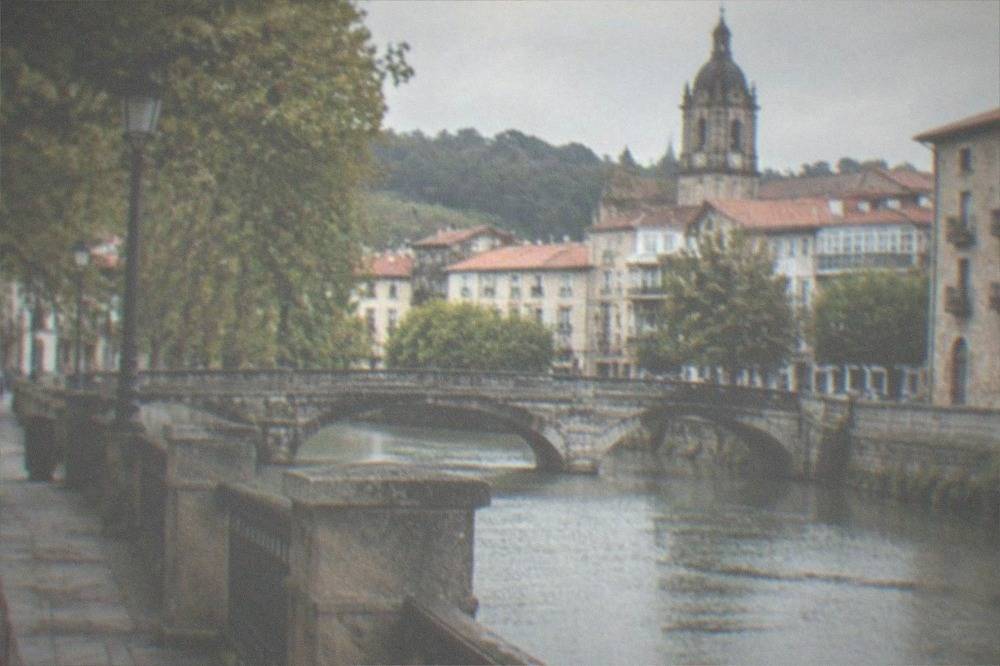 A peaceful present-day street in Gernika with stone buildings and the tower of a church above the rooftops