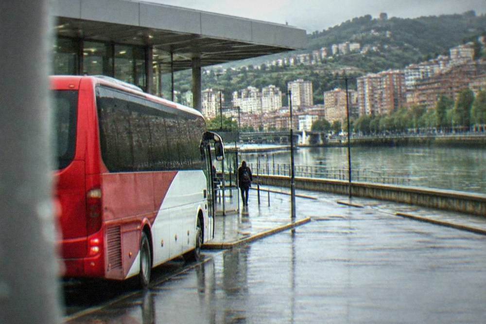 A red and white Bizkaibus airport bus parked at a kerb outside a terminal building