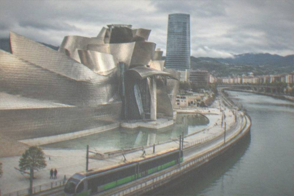 A green and silver Bilbao tram passing the Guggenheim Museum along the riverside boulevard