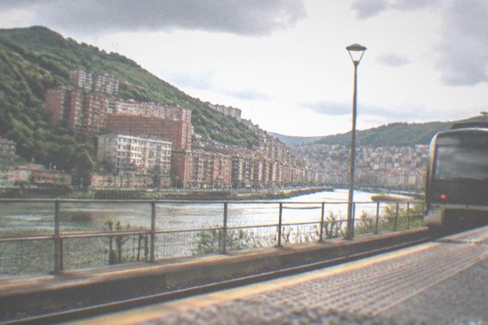 An Euskotren train at a small coastal station platform near green hills