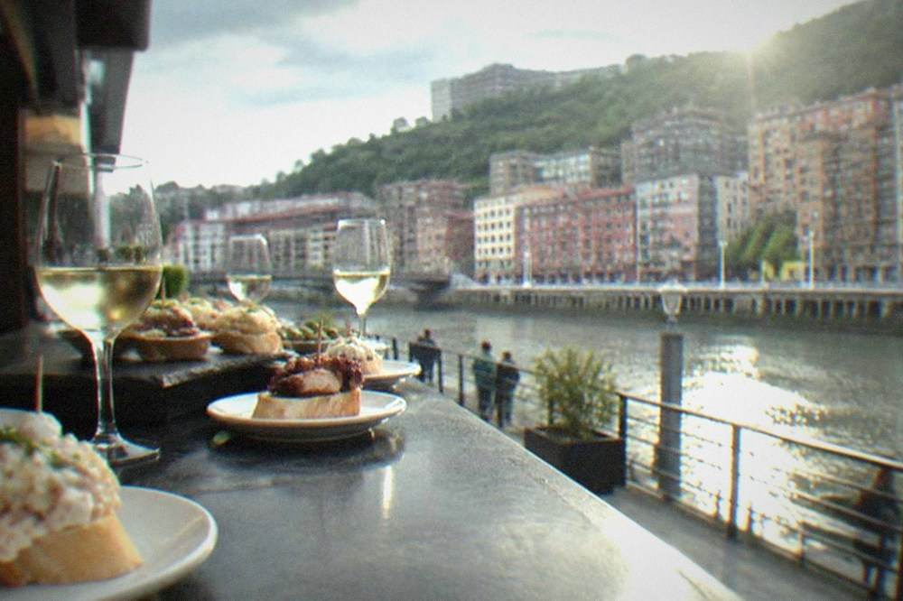 A pintxos bar counter in Bilbao crowded with small plates and glasses of txakoli wine