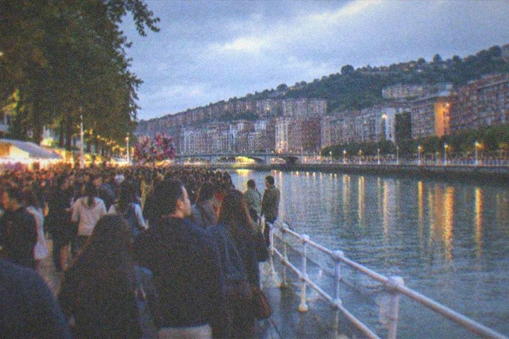 A crowded plaza in Bilbao during an evening festival with lights and street vendors