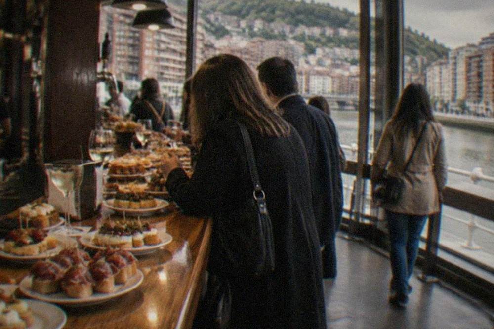 A counter covered with small pintxo plates and glasses of txakoli wine in a crowded Bilbao bar