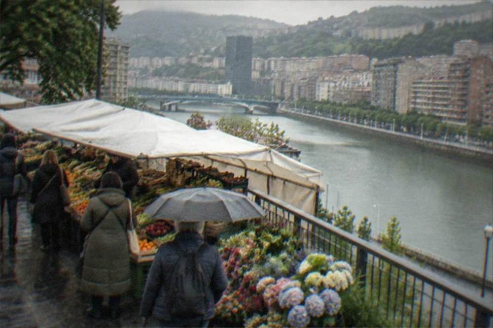 People browsing an outdoor market stall with produce and flowers in central Bilbao