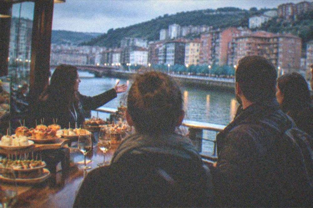 A small group with a guide standing at a busy pintxos bar counter in Bilbao in the evening