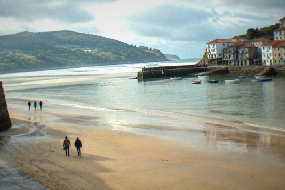 A wide sandy estuary beach at low tide with green hills behind and a few people walking