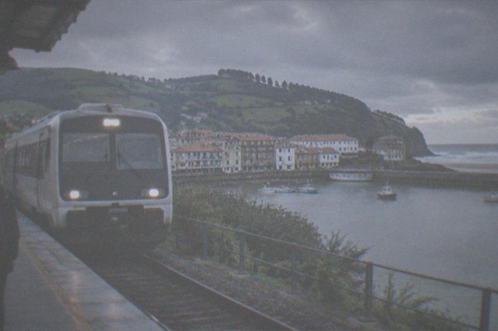 A train pulling into a small countryside station platform with green hills behind it