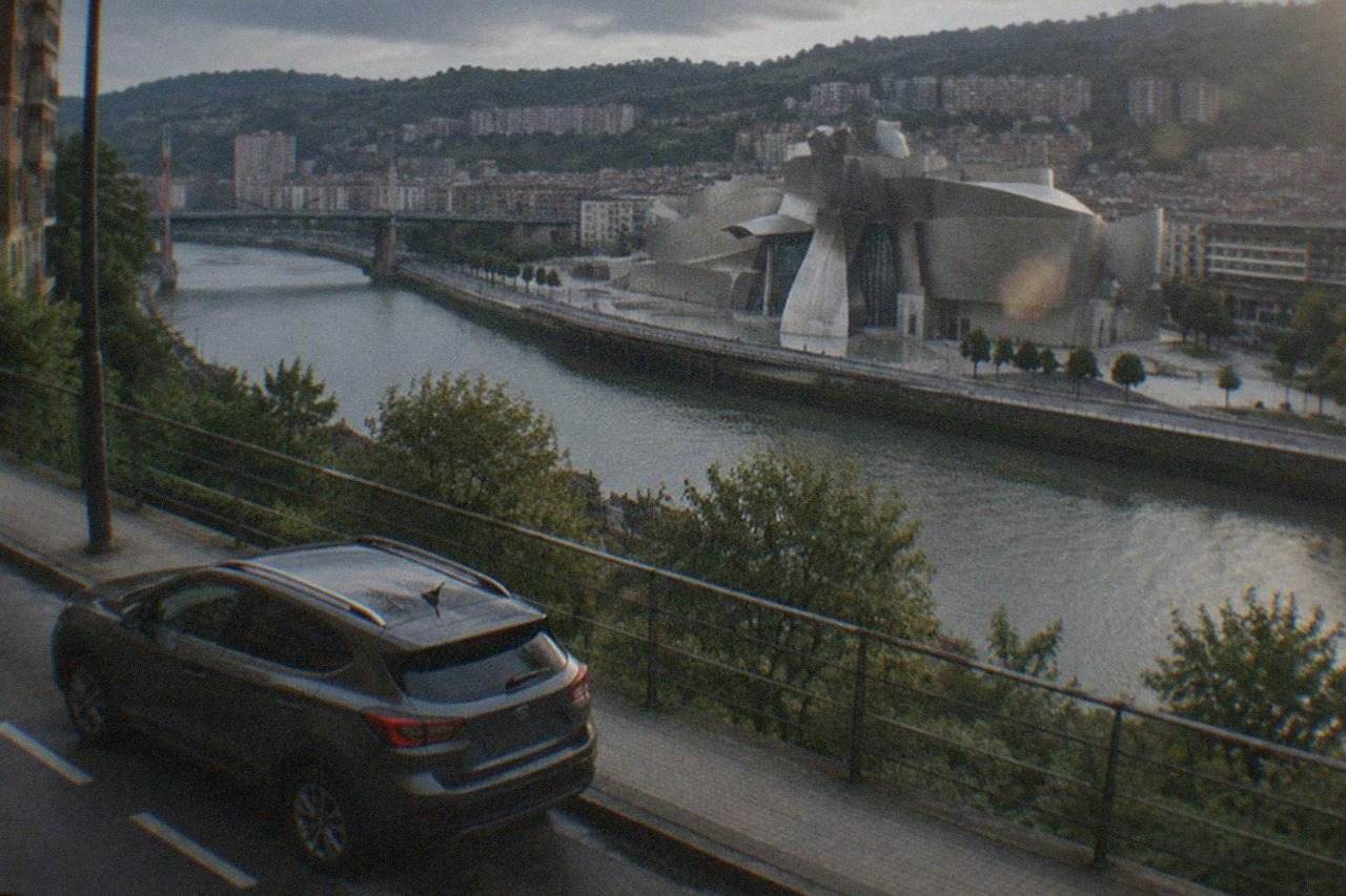 A rental car parked on a Bilbao street with the Guggenheim Museum's titanium curves visible across the river