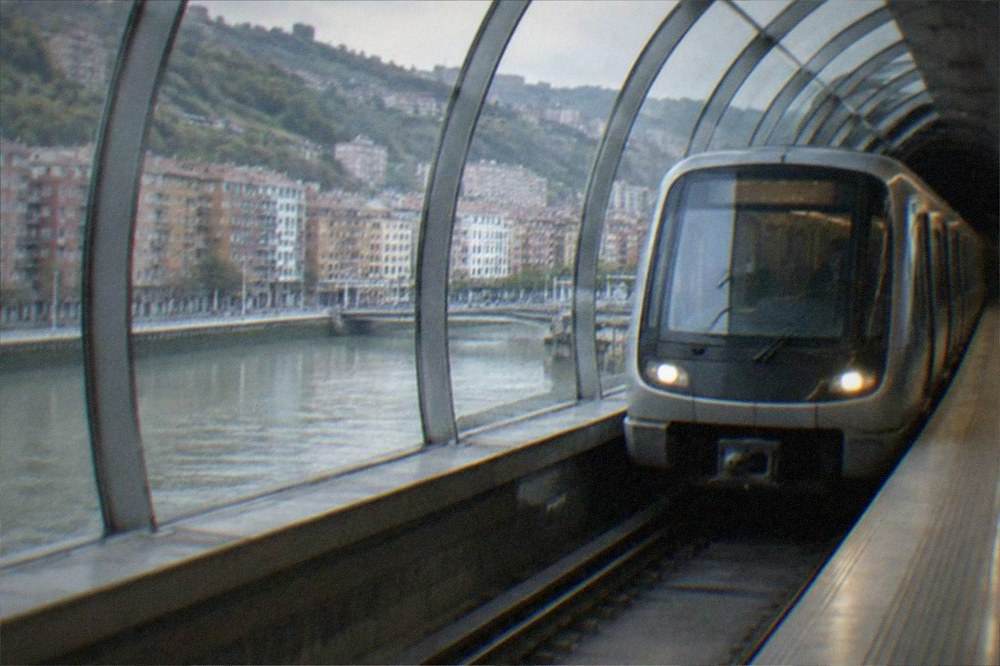 A metro train arriving at an underground Bilbao station with a curved Foster-designed canopy
