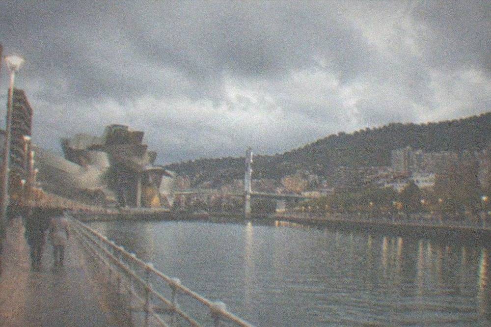 Illuminated riverside promenade in Bilbao with people walking in the evening