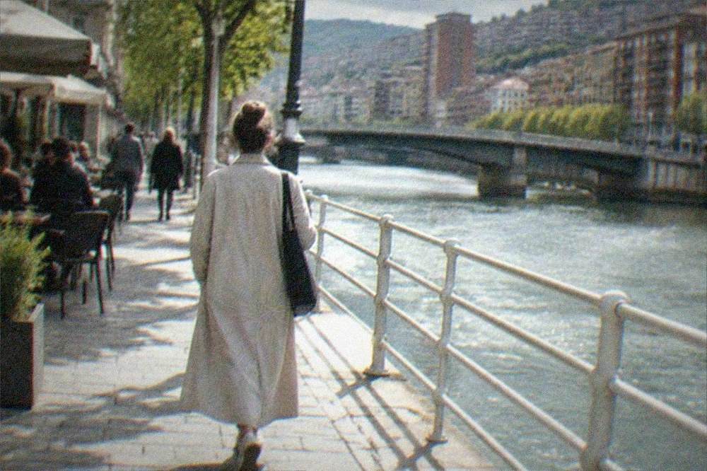 A woman walking alone through a lit evening street in central Bilbao with people at outdoor tables