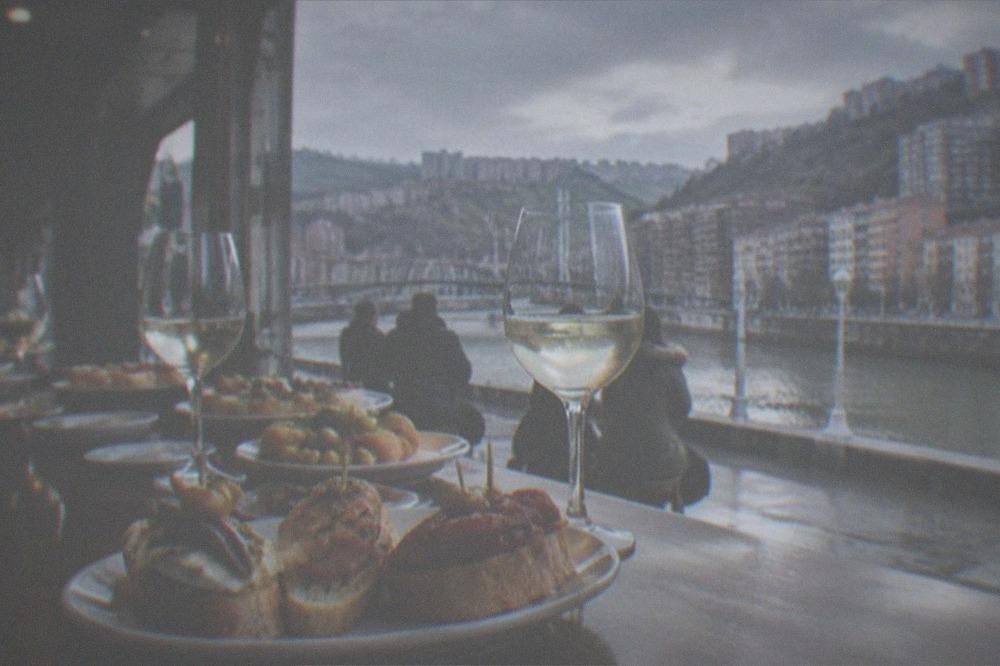 A pintxos bar counter in Bilbao crowded with small plates and glasses of txakoli