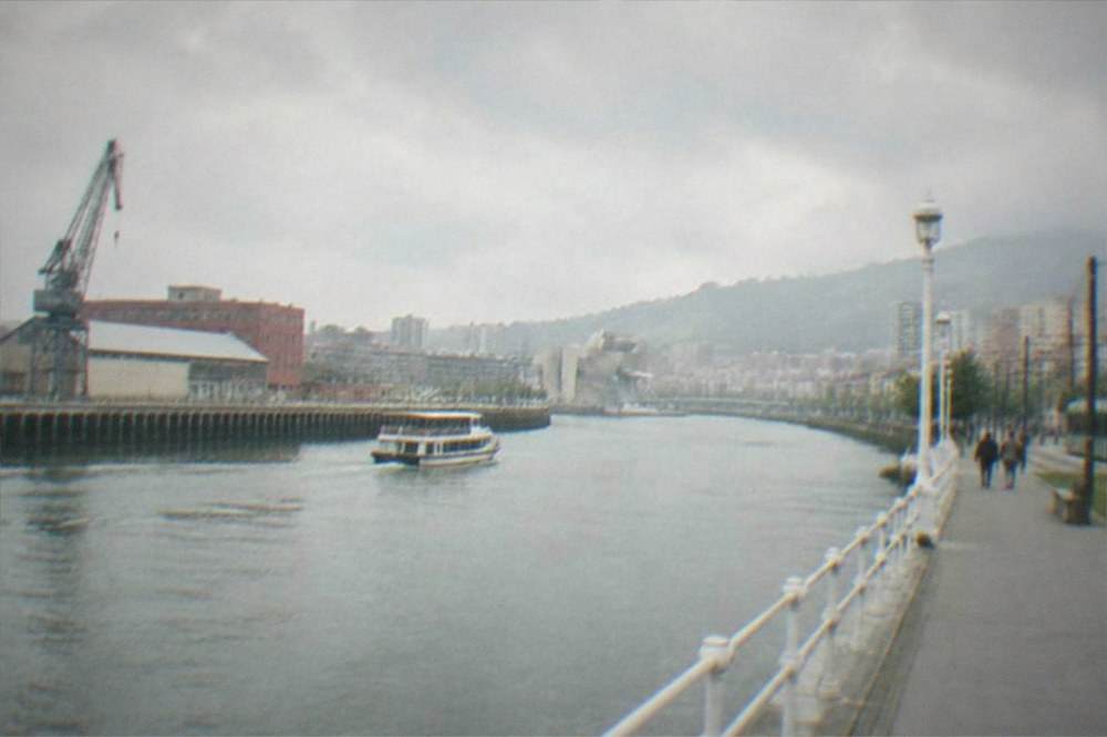 The Nervion riverfront in Bilbao under an overcast Atlantic sky with the tram line alongside