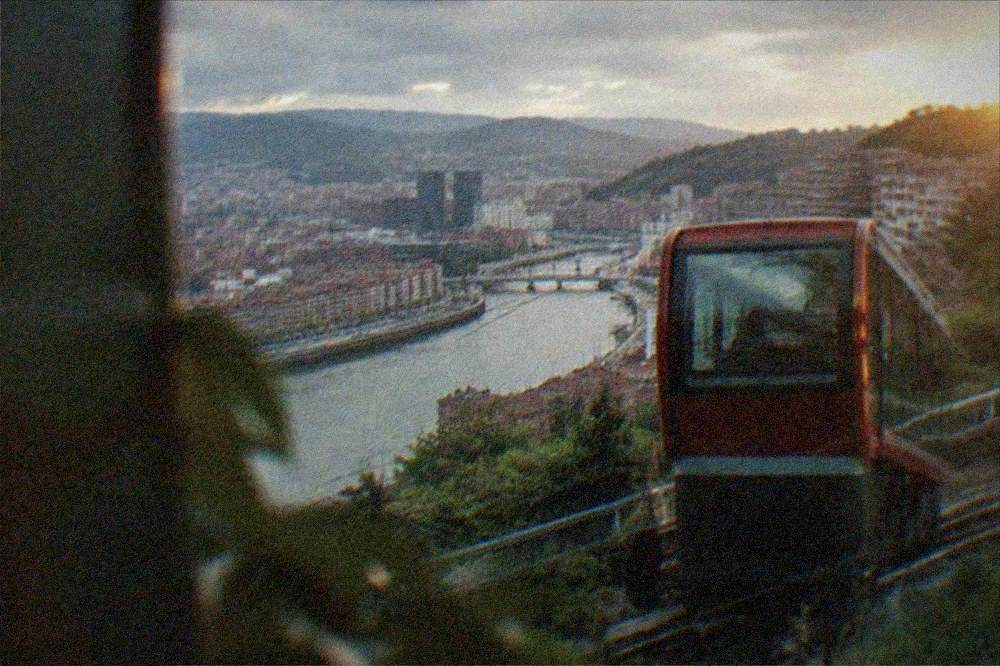 Cable funicular car climbing the hillside above the illuminated Bilbao skyline at dusk