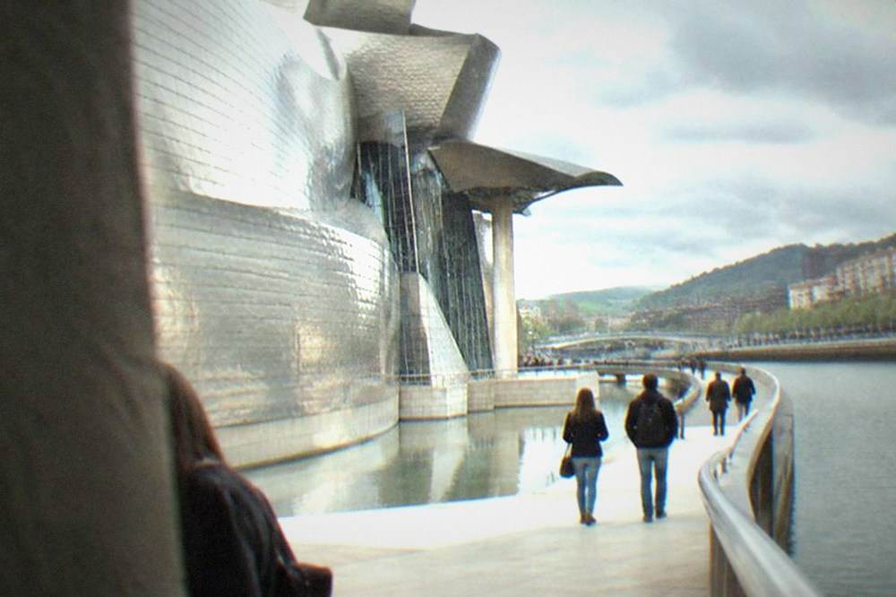 Visitors walking beside the shallow reflecting pool and titanium panels at the Guggenheim Museum in Bilbao