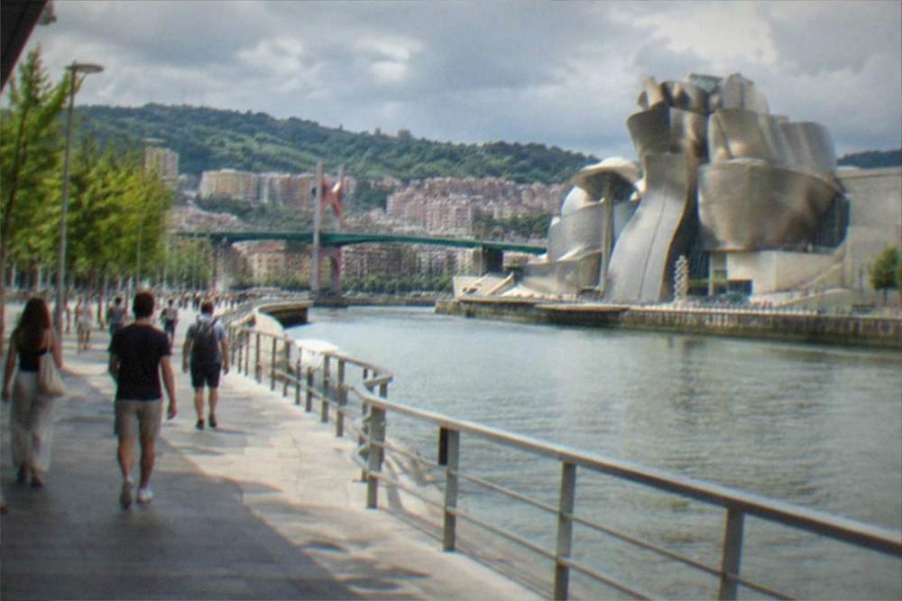 The Bilbao riverfront in summer with people walking along the estuary promenade toward the Guggenheim