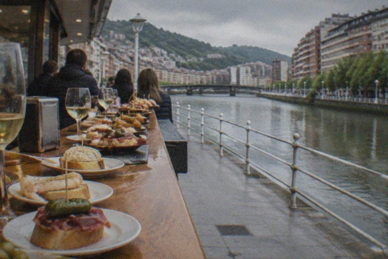 A pintxos bar counter in Bilbao crowded with small plates and glasses of txakoli wine