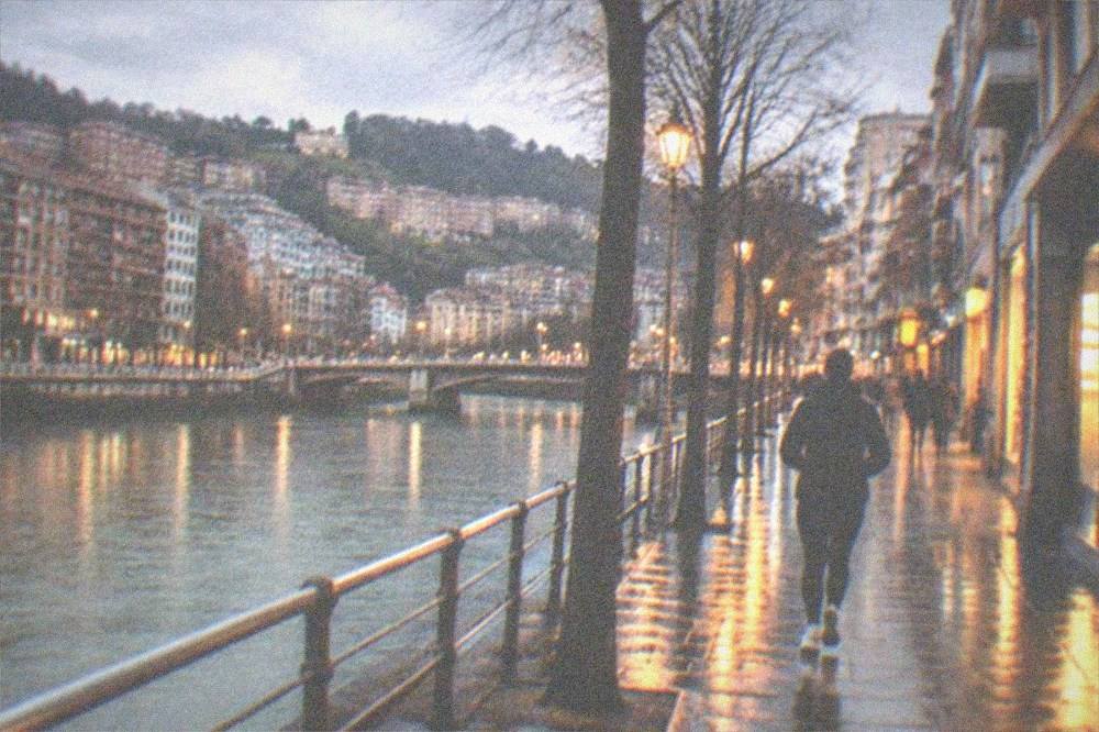 A quiet Bilbao street with lit shopfronts and wet pavements on a winter evening