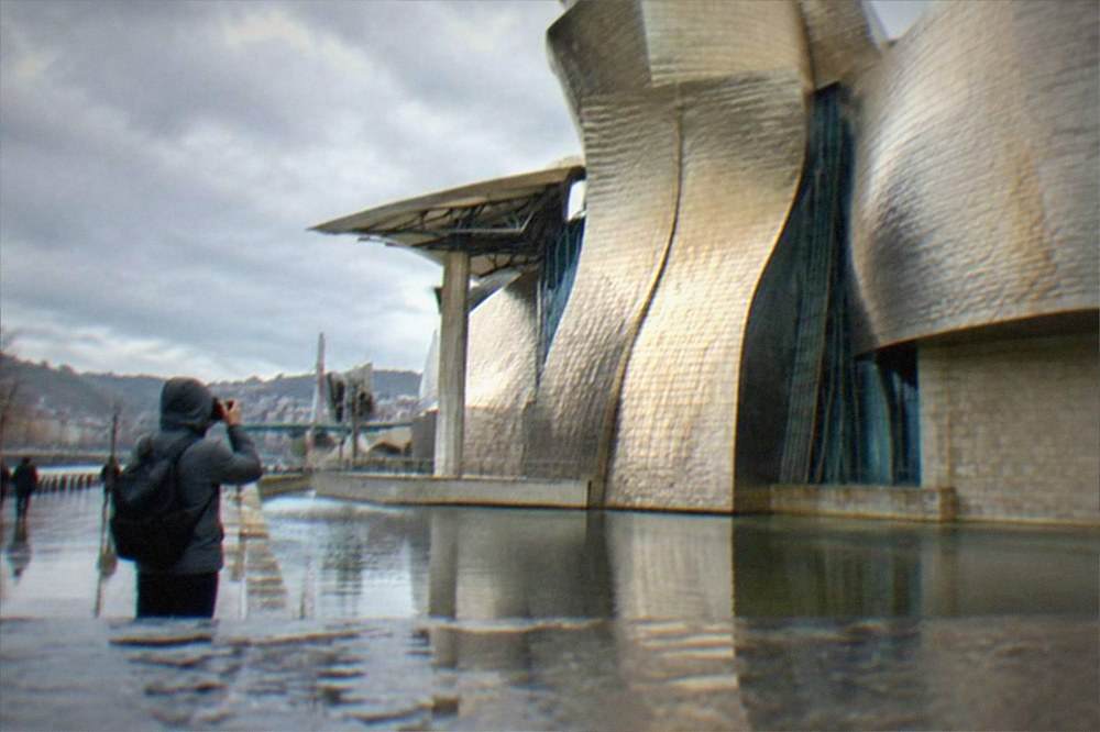 A visitor in a rain jacket photographing the Guggenheim Museum under low winter cloud