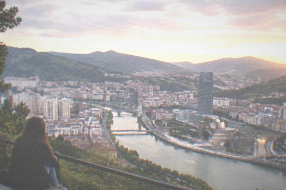A hilltop viewpoint above Bilbao at sunset with the estuary winding through the city and hills beyond
