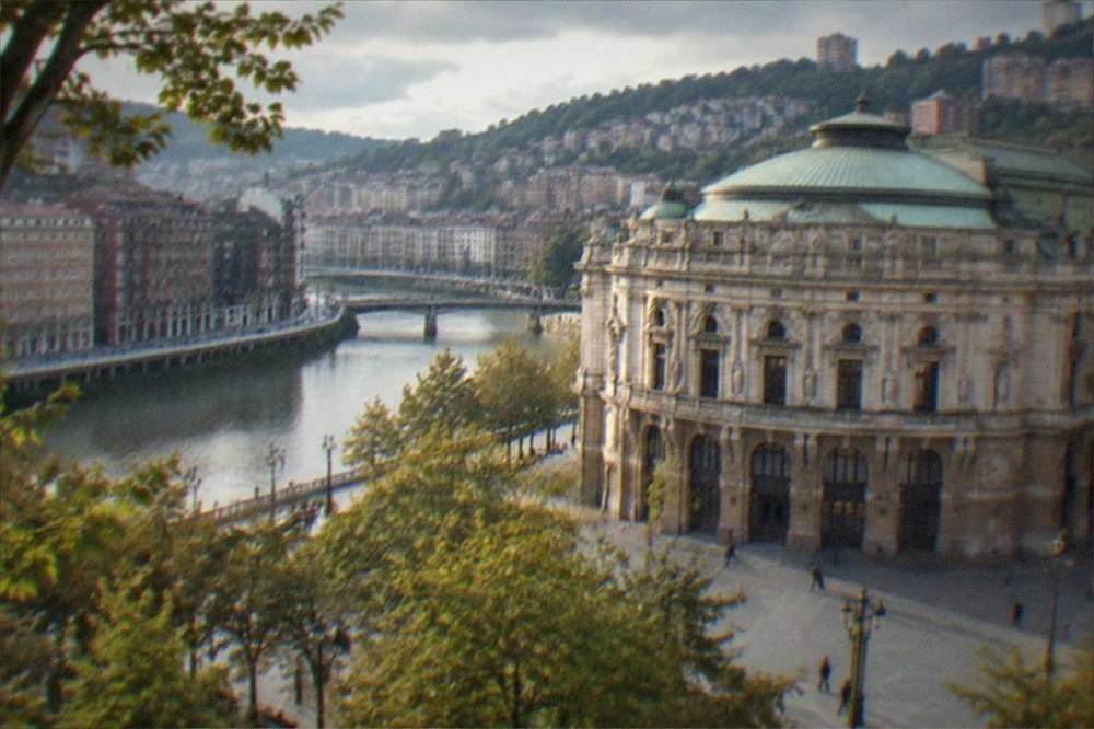 A grand theatre facade with ornate stonework photographed from a tree-lined square in Bilbao