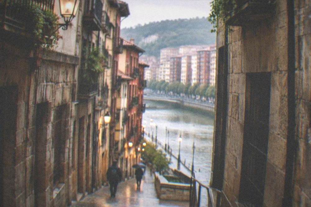 A narrow medieval street in Bilbao's old town with worn stone buildings and warm late-afternoon light