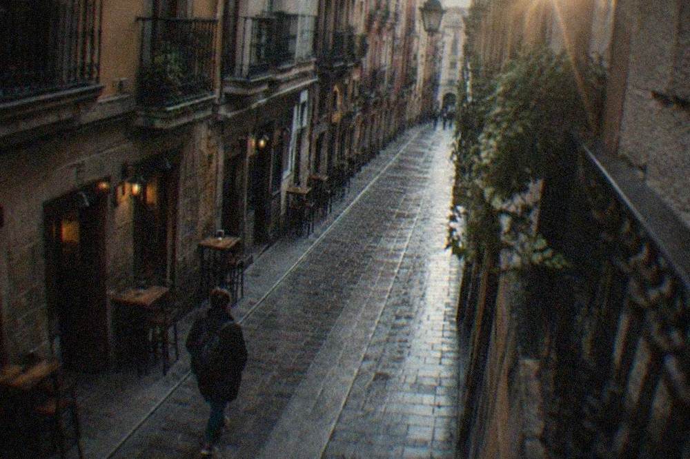 A narrow medieval street in Bilbao's Casco Viejo with a traveler walking alone past small bars