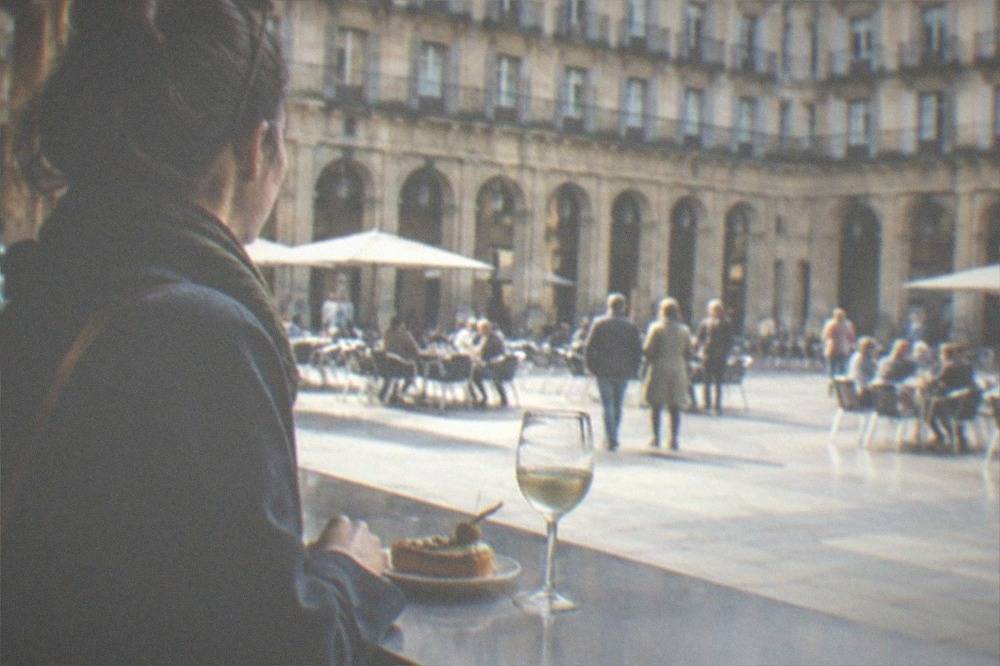 A traveler standing at a pintxos bar counter in Plaza Nueva with a small plate and a glass of txakoli