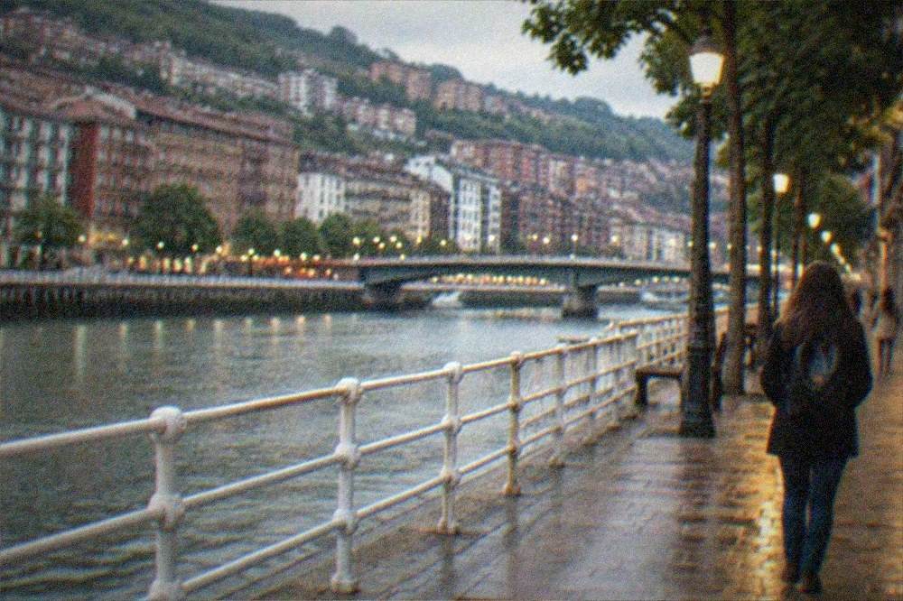 A traveler walking alone in the evening through a lit pedestrian street in central Bilbao