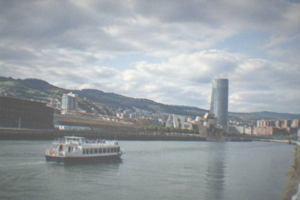 A small boat cruising on the Nervion estuary with the city skyline behind it