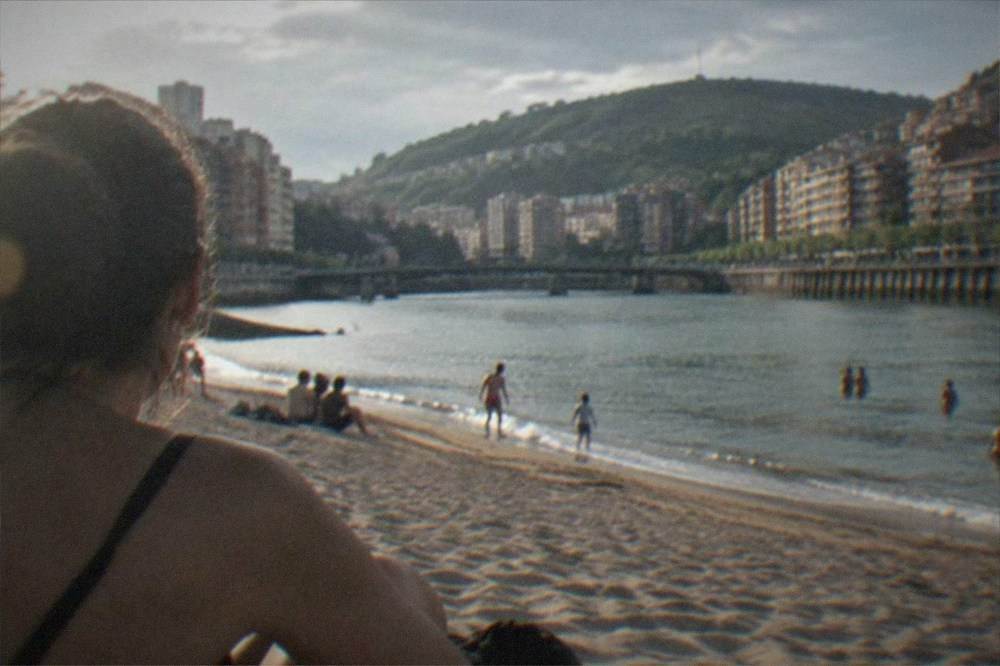 A sandy beach with gentle waves and a few swimmers on a sunny summer day