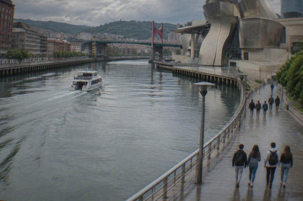 Teenagers walking along the Nervion riverfront in Bilbao with the Guggenheim Museum titanium curves behind them