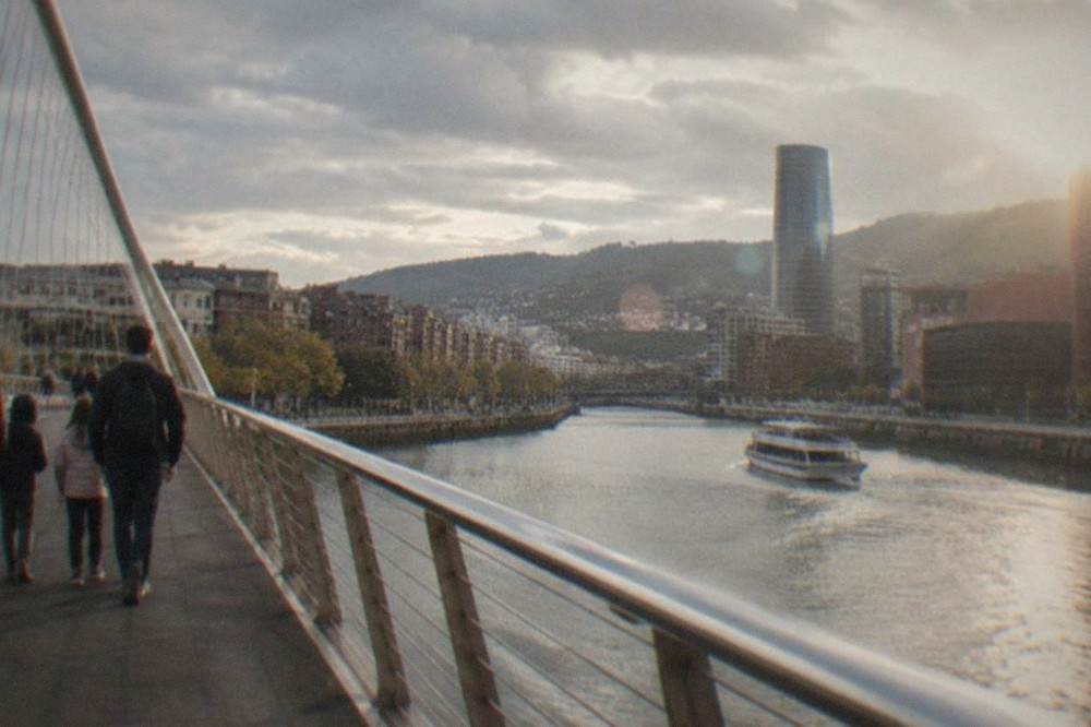 A family group crossing Zubizuri bridge over the Nervion river on a bright morning in Bilbao