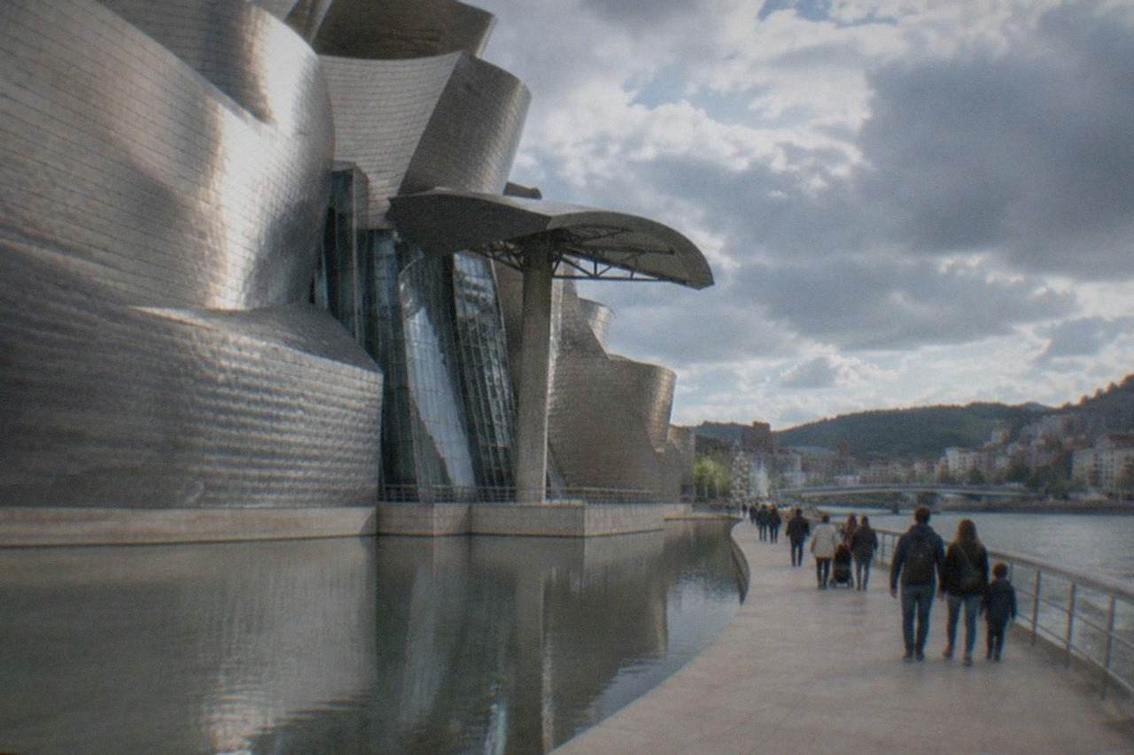Families walking along the riverside promenade beside the Guggenheim Museum in Bilbao on a bright day
