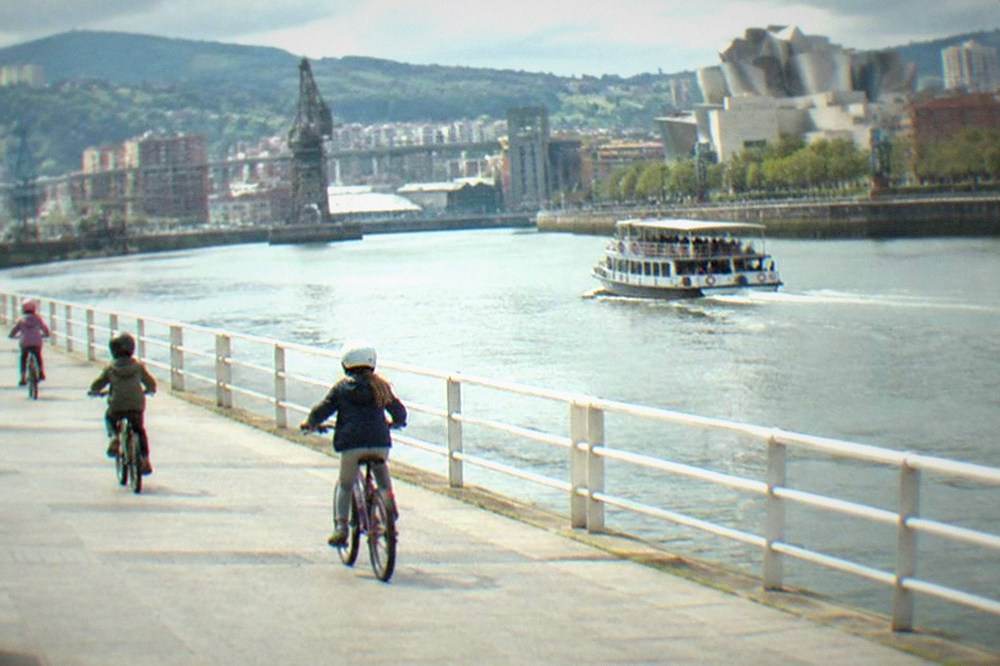 Children on bicycles riding along the wide flat riverside path beside the Nervion estuary in Bilbao