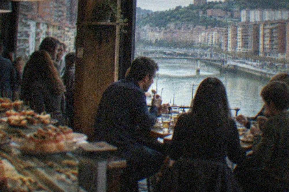 A family sharing food and drinks at a small table in a lively Bilbao pintxos bar in the evening